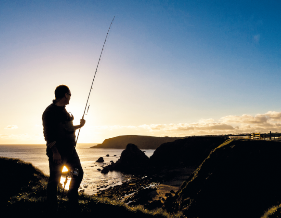 Silhoutte of a man about to start fishing from the rocks