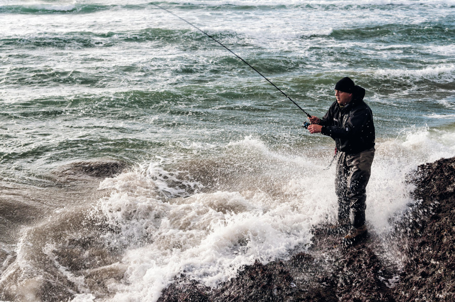 Man fishing on rocks with the sea waves hitting 