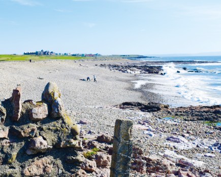 Two fishermen try their luck at a small bay close to Porthcawl. Distant view of Royal Porthcawl Golf Course.