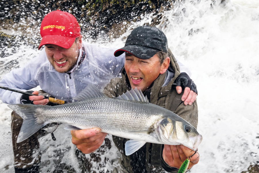 two men posing for a catch picture with wave crashing into the back of them.