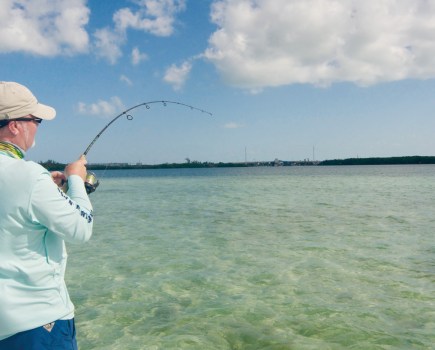 man standing in shallow clear ocean playing a fish