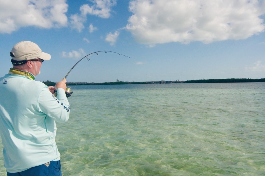 man standing in shallow clear ocean playing a fish